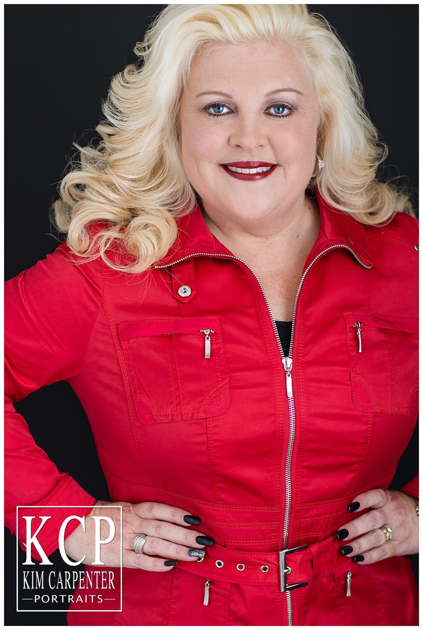 A close photograph of a woman wearing a bright red jacket with her hands on her hips. Lakeland Photographer, professional headshots