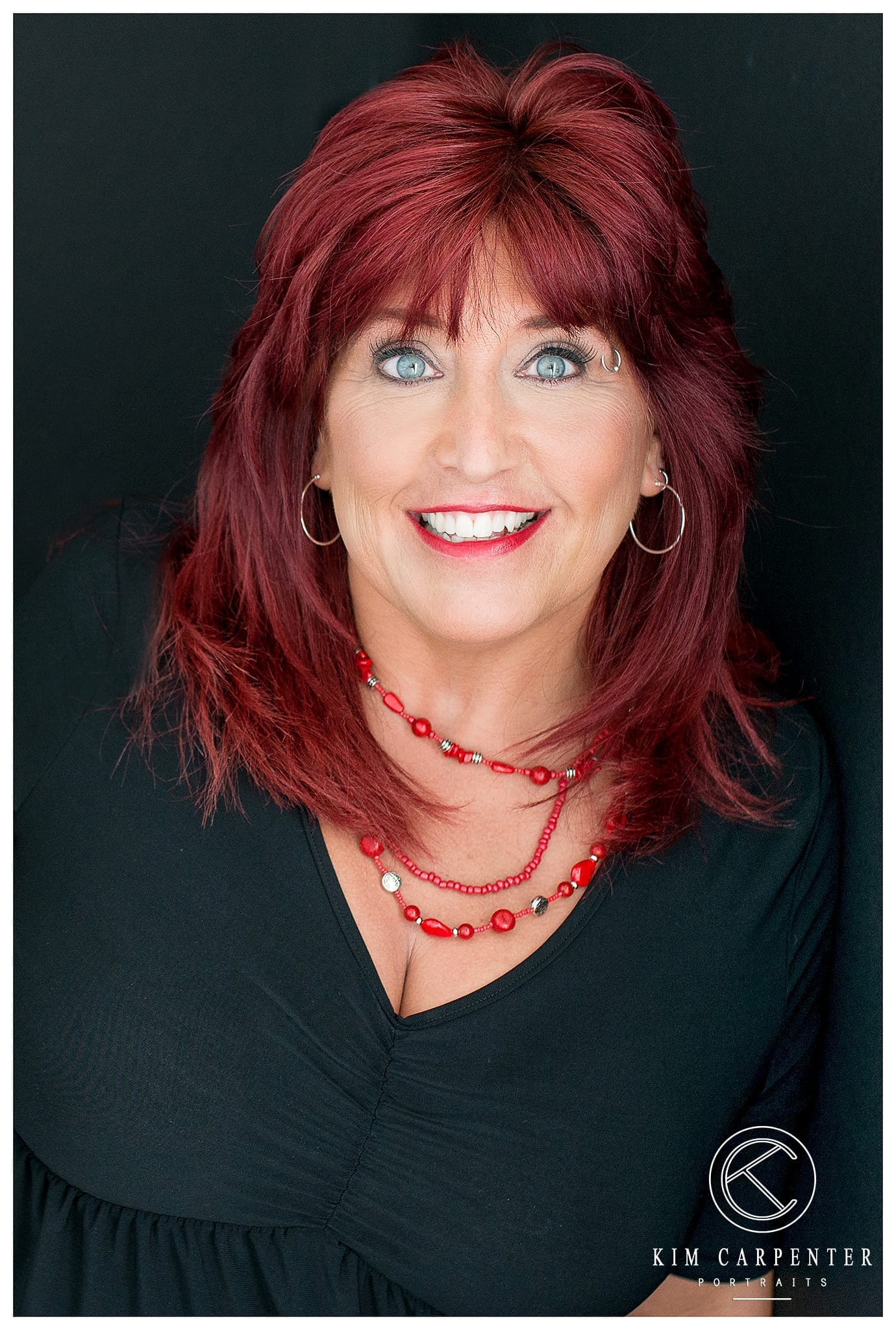 Woman smiling at camera with a black shirt and red necklace. Lakeland Photographer, professional headshots