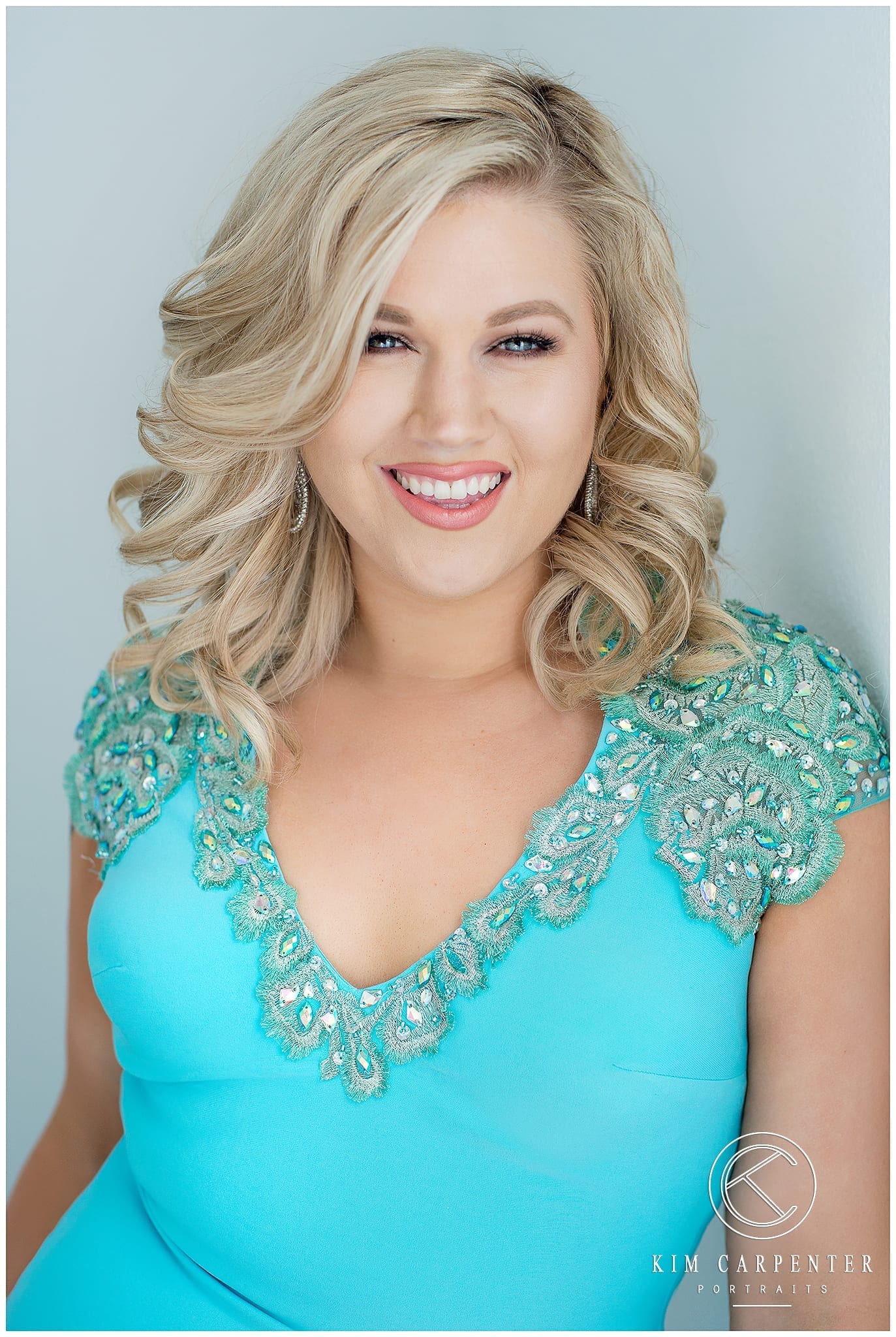 Woman smiling and posing for camera with blonde curls and a blue dress. Lakeland Photographer, professional headshots