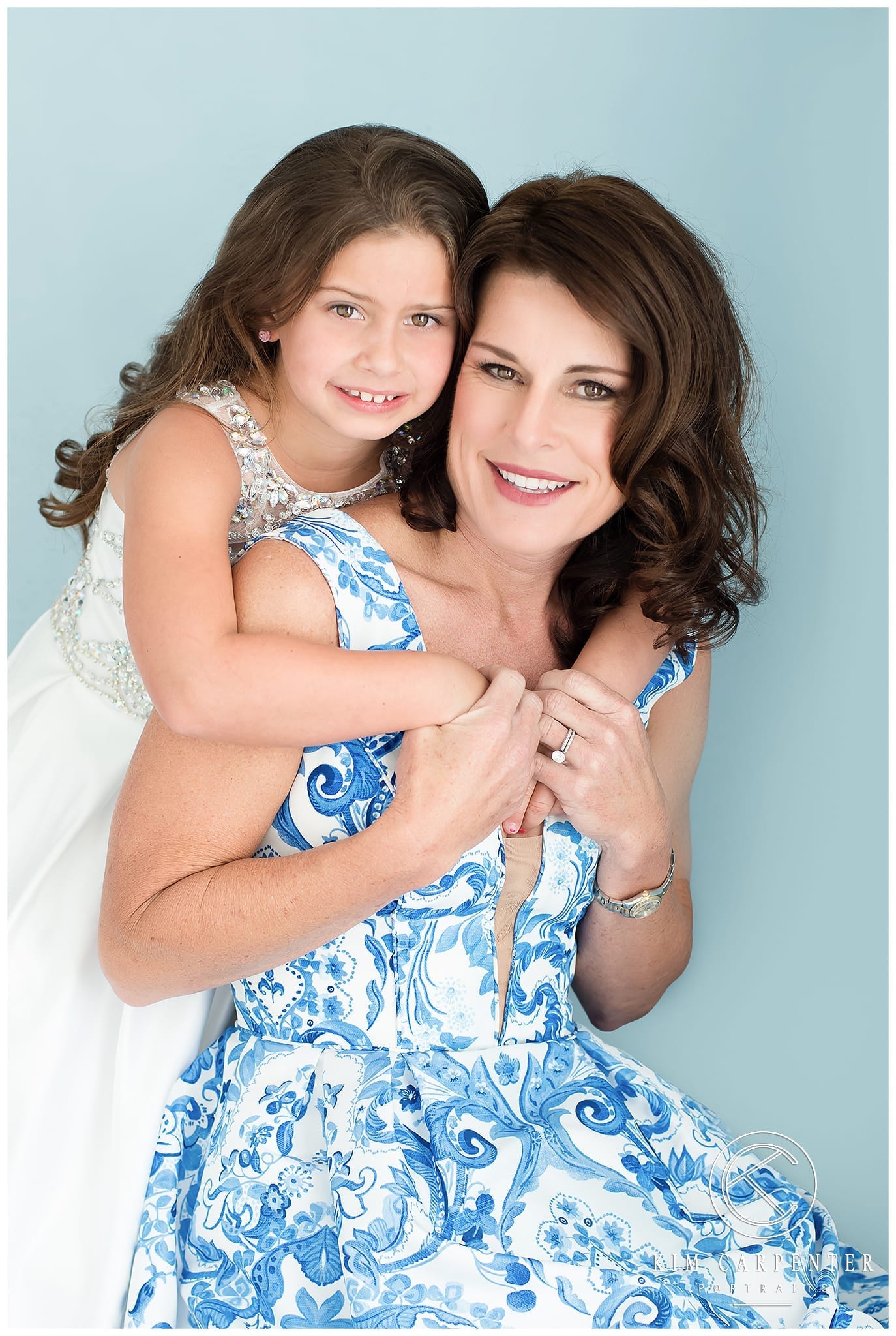 Lakeland Photographer - Mother and daughter hugging each other in blue and white dresses with a blue background