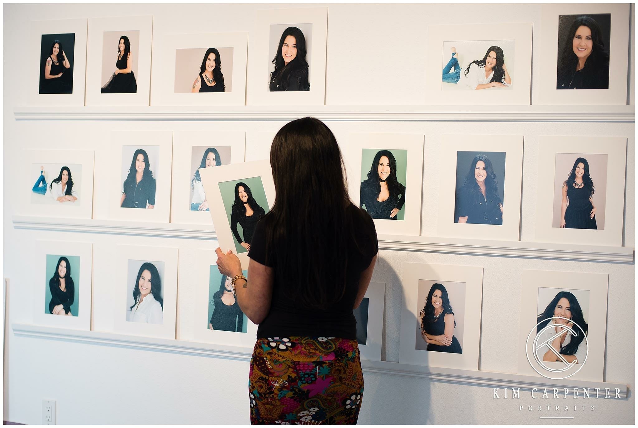 A woman standing and looking at professional headshots on shelves.
