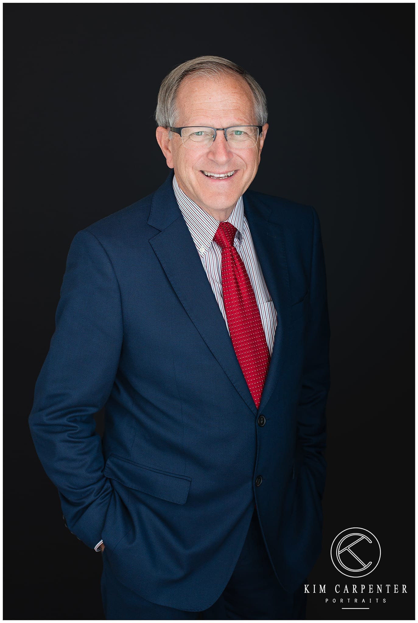 Man standing with a black background and wearing glasses. Lakeland Photographer, professional headshots