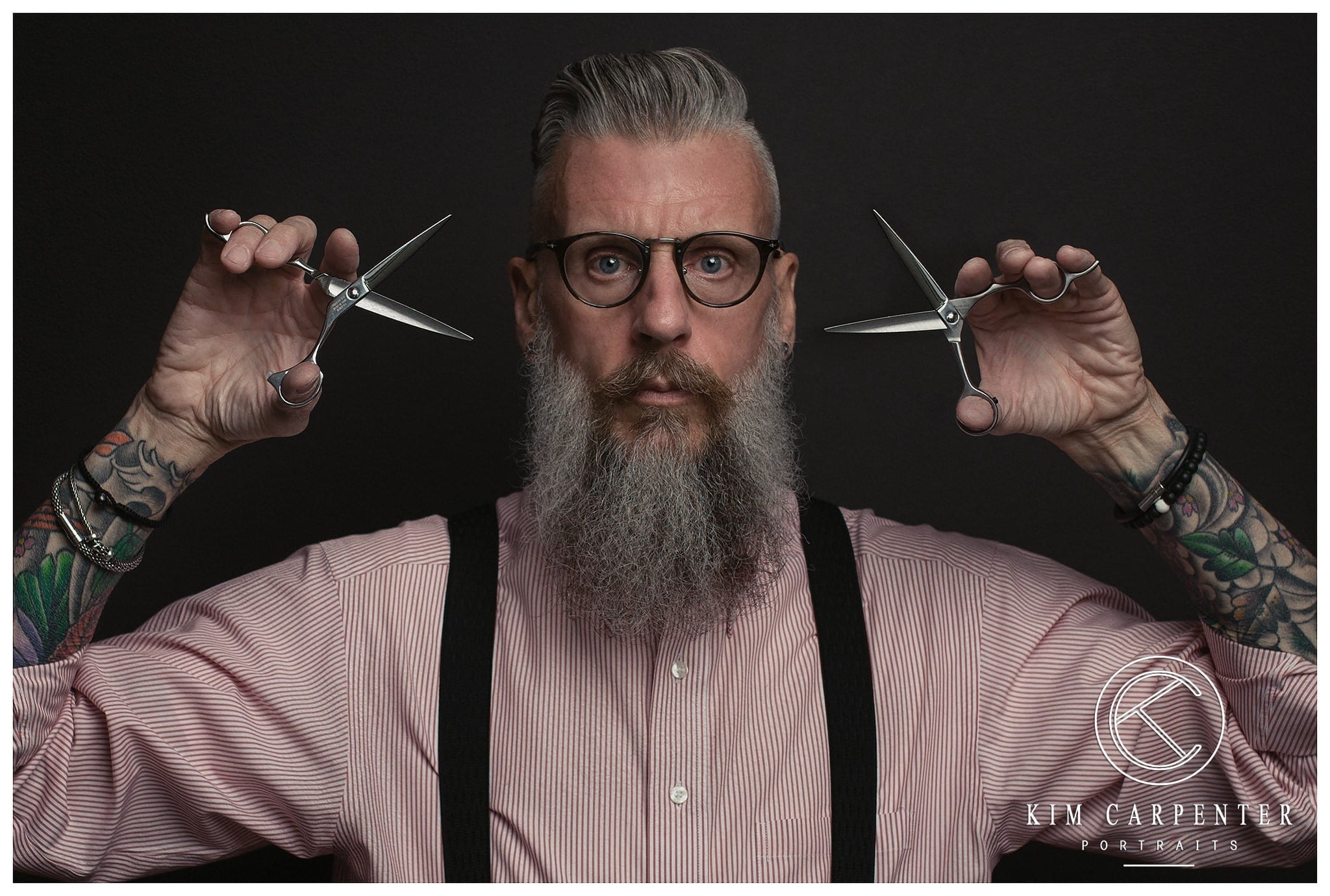 Man holding two pairs of hair cutting scissors.