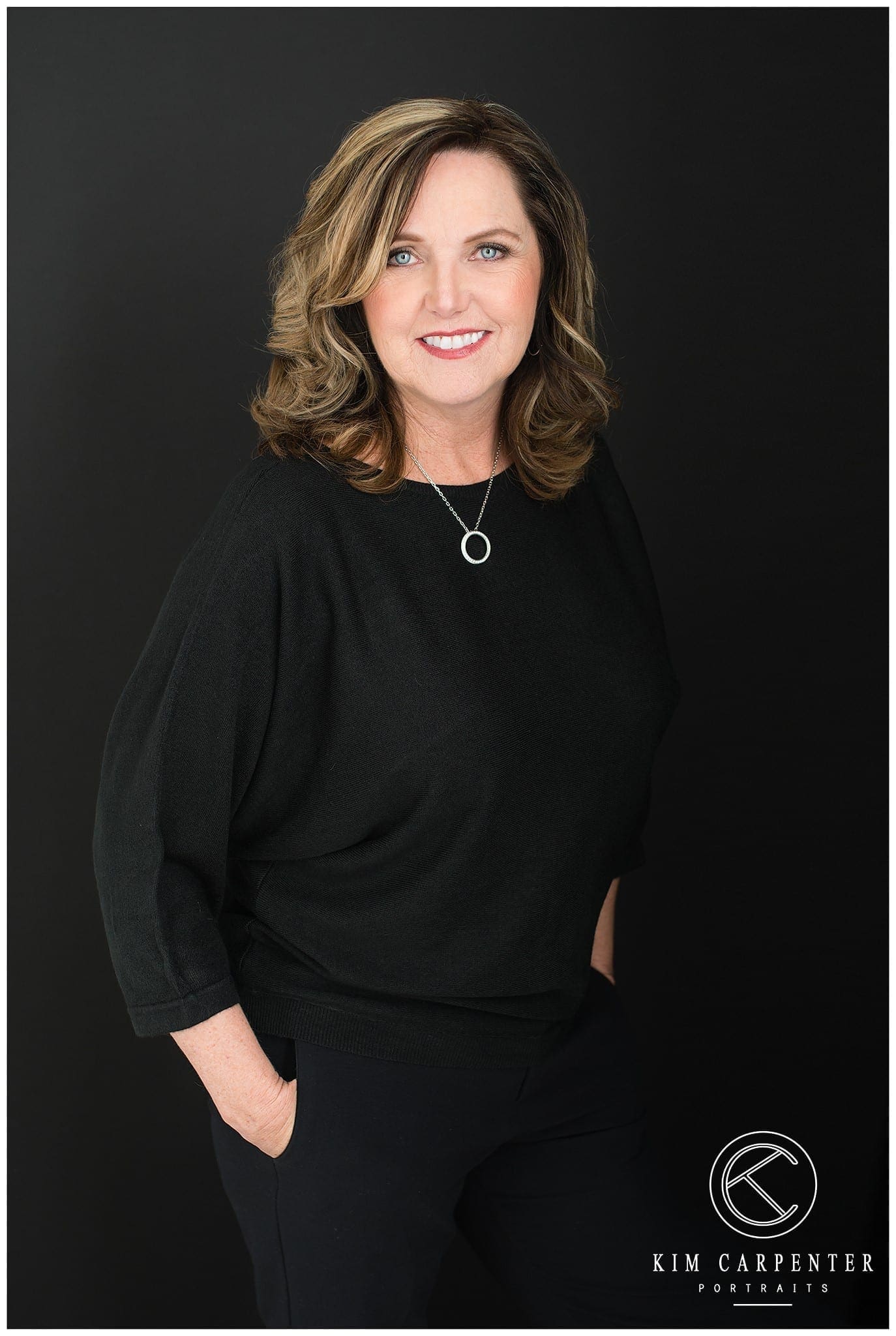 Woman wearing black standing in front of a black background. 